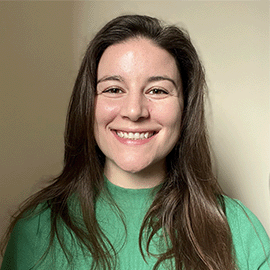 A young woman wearing a bright green jumper smiles at the camera in front of a beige background.